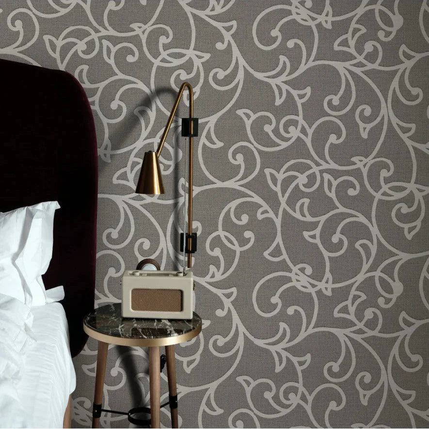 Decorative Erismann wallpaper with intricate pattern, side table with lamp, and bed in the foreground.