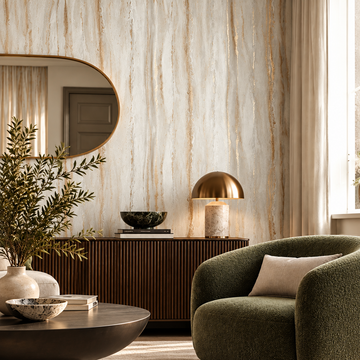 A styled interior scene featuring a rounded olive green upholstered accent chair with a beige pillow, set in a room with textured beige and gold vertical-vein wallpaper, a dark wood credenza, a gold dome table lamp, and a dark round coffee table.