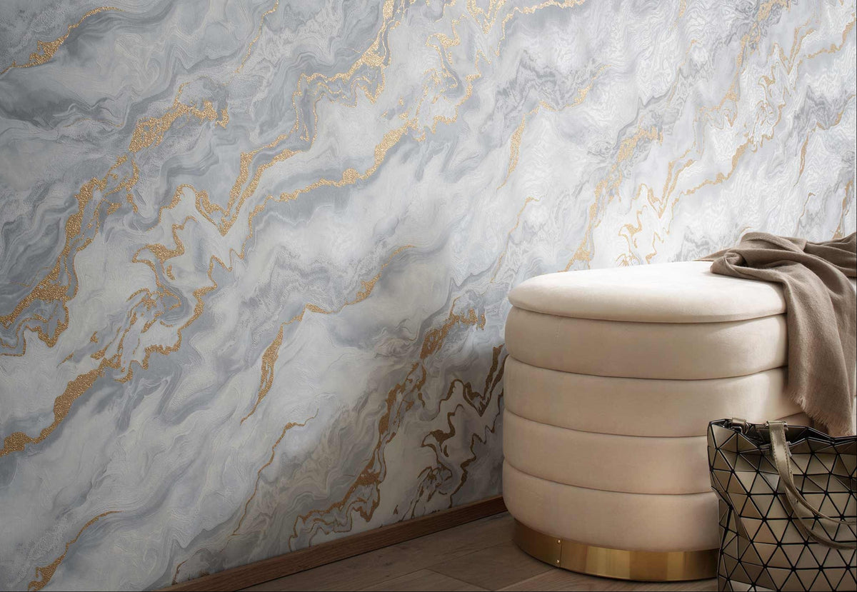 Erismann Elle Decoration 4 marble effect wallpaper in soft grey tones with gold accents styled in a modern interior with upholstered ottoman