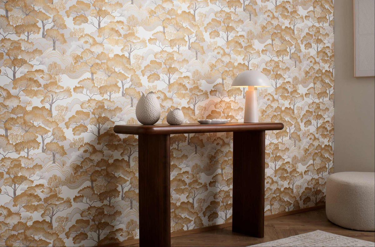 Erismann Elle Decoration 4 scenic tree wallpaper in warm golden tones styled in a modern interior with wooden console table and decorative accents
