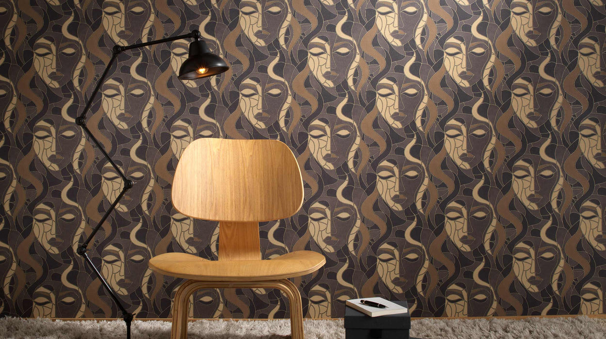 Erismann Elle Decoration abstract face wallpaper in brown and gold tones styled with a wooden chair and modern floor lamp in an interior setting