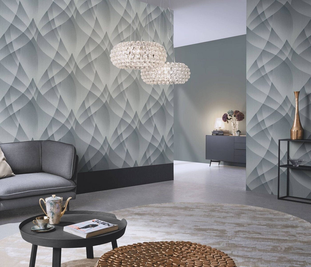 Erismann Fashion For Walls 4 10374-29 wallpaper in a modern lounge with a geometric feature wall, curved sofa, round coffee table with tea set and magazine, bubble pendant lights, sideboard with lamp and vases, and a calm contemporary feel.