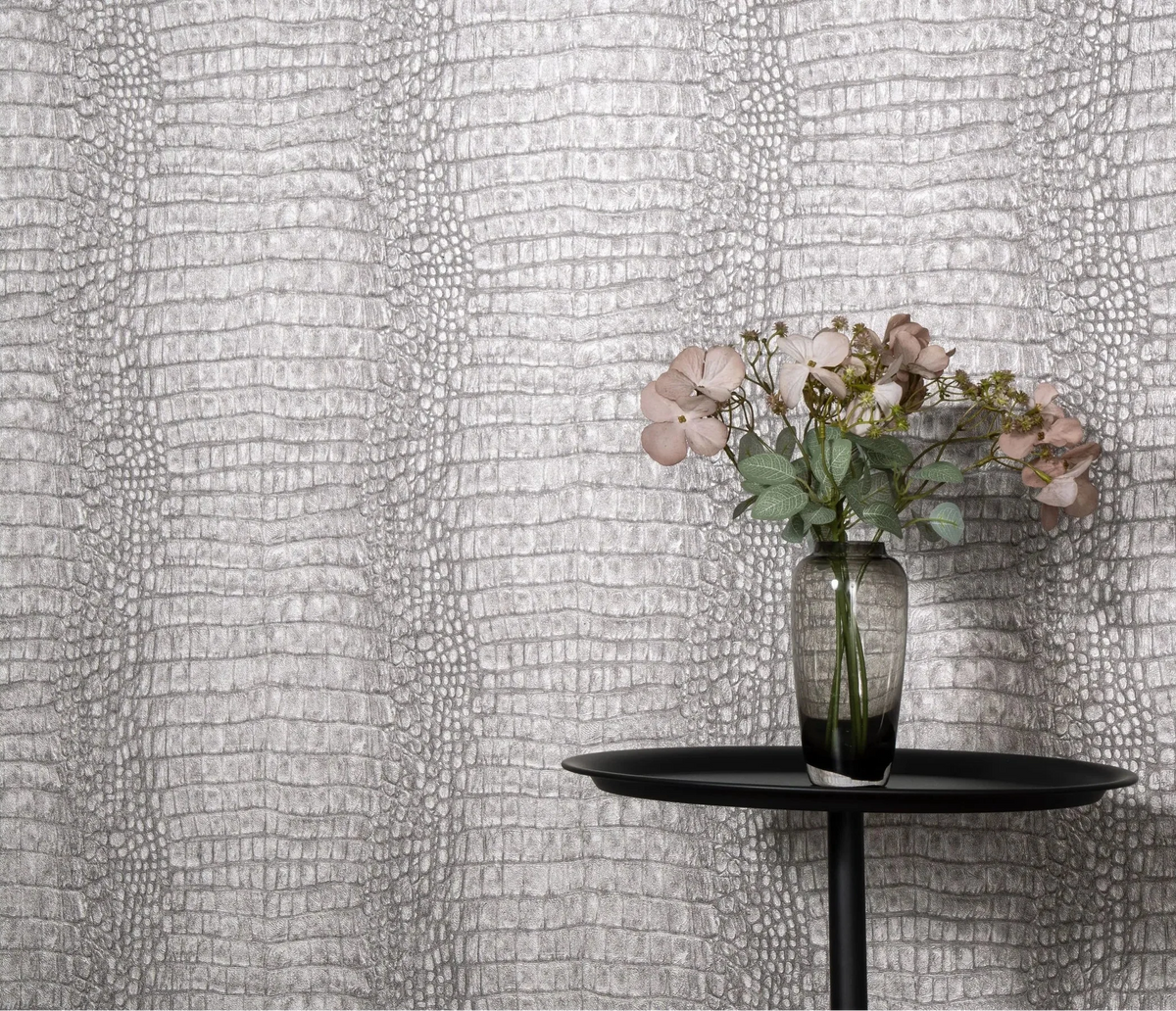 Erismann Forest Dreams 10560-37 wallpaper on a textured grey reptile-skin patterned wall behind a black round table and flower vase.