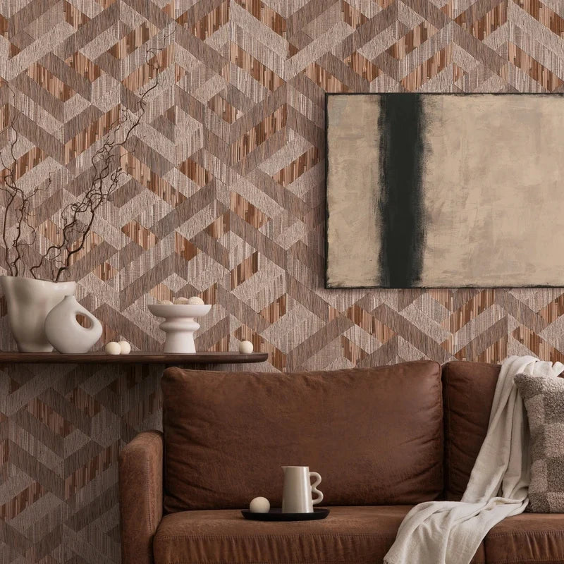 Marburg Boho 35789 Geometric brown and taupe wallpaper with interlocking angled bands and fine vertical striations, shown behind a brown leather sofa with a pillow and throw, a floating shelf with white ceramic vases and branches, small decorative spheres, a mug on a tray, and a.