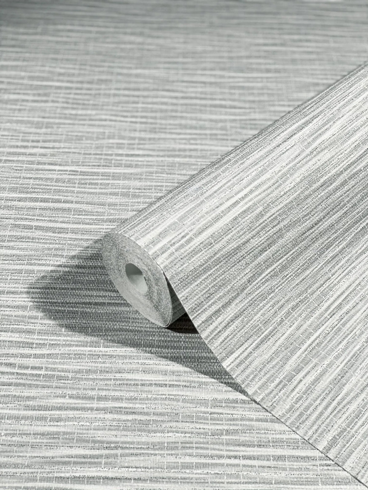 Marburg Botanica 33323 A gray textured wallpaper roll with fine horizontal striations resting on the same patterned sheet.