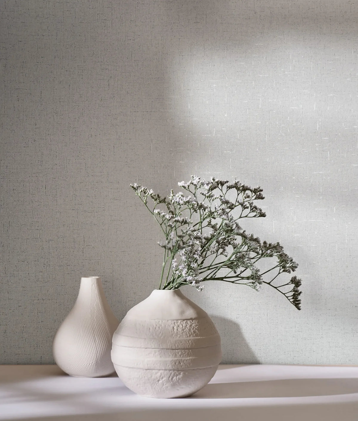 Marburg City Romance 35109 Light gray crosshatched wallpaper behind two white ceramic vases, one holding small white flowers, with soft shadows across the scene.