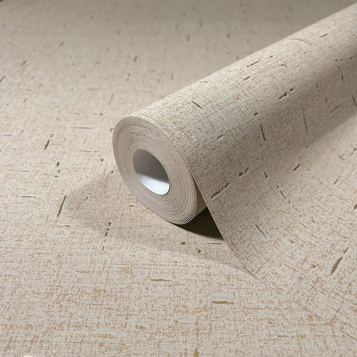 Marburg City Romance 35112 Close-up of a beige wallpaper roll on matching unrolled wallpaper, showing a fine linen-like texture with scattered short linear flecks.
