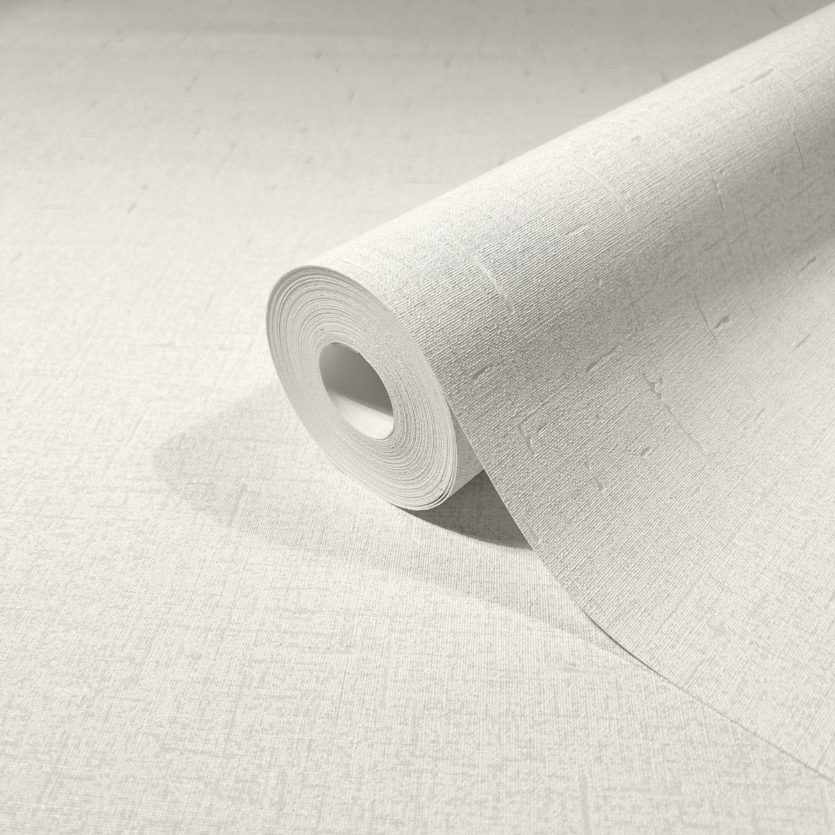 Marburg City Romance 35115 A close-up of a wallpaper roll partially unrolled on a matching light textured surface, showing a subtle crosshatch with small linear dash details.
