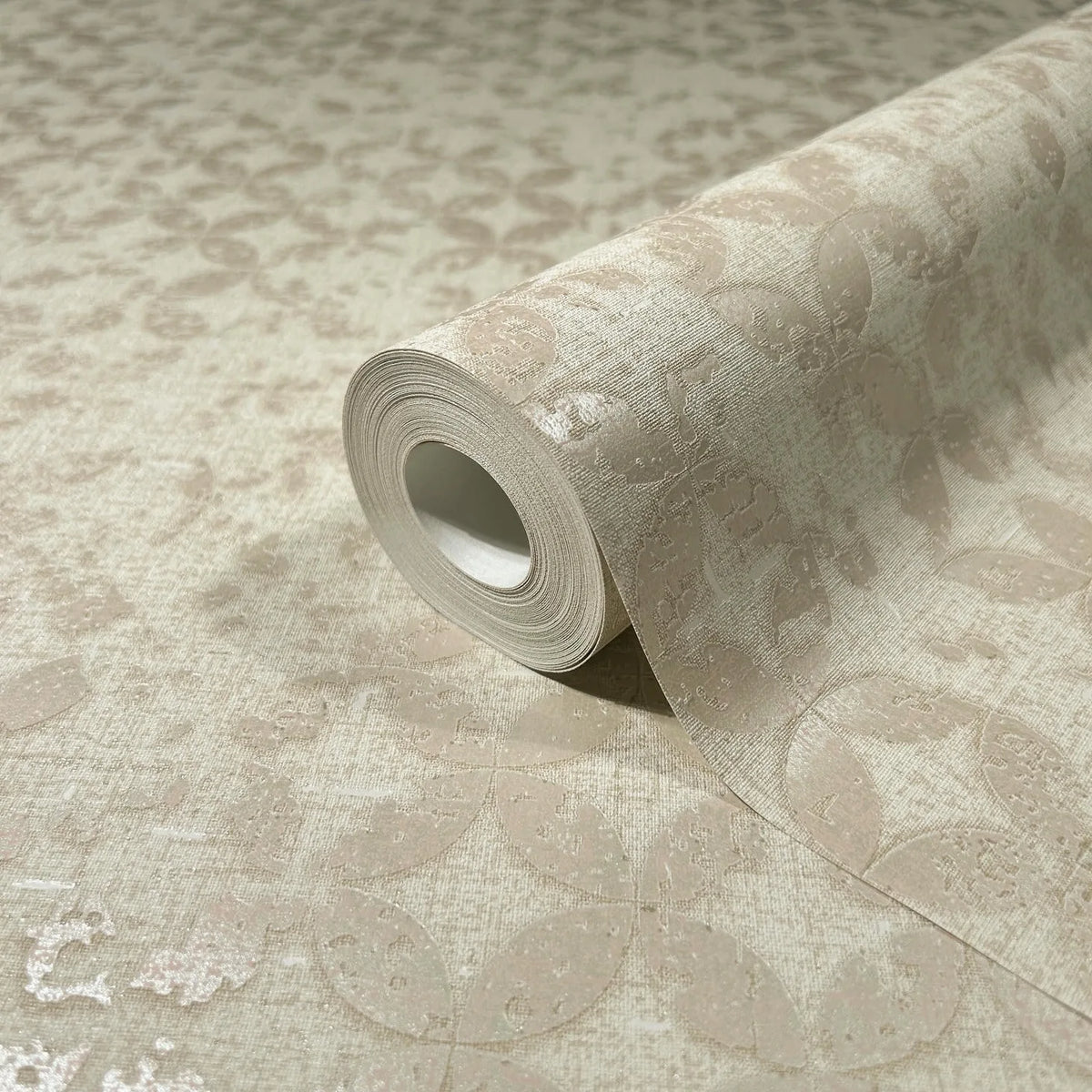 Marburg City Romance 35117 A beige wallpaper roll resting on a matching unrolled sheet, showing a subtle tonal oval or leaf pattern with a slight sheen.