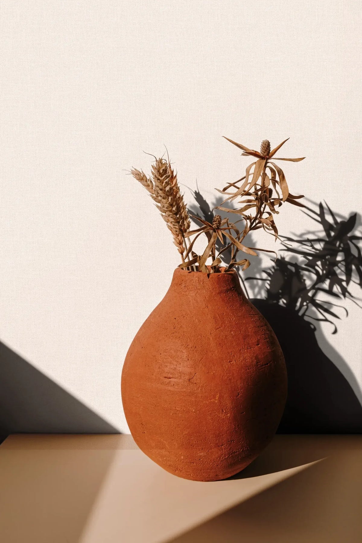 Marburg 47607 wallpaper lounge feature wall with a shelf and terracotta vase of dried stems casting soft shadows.