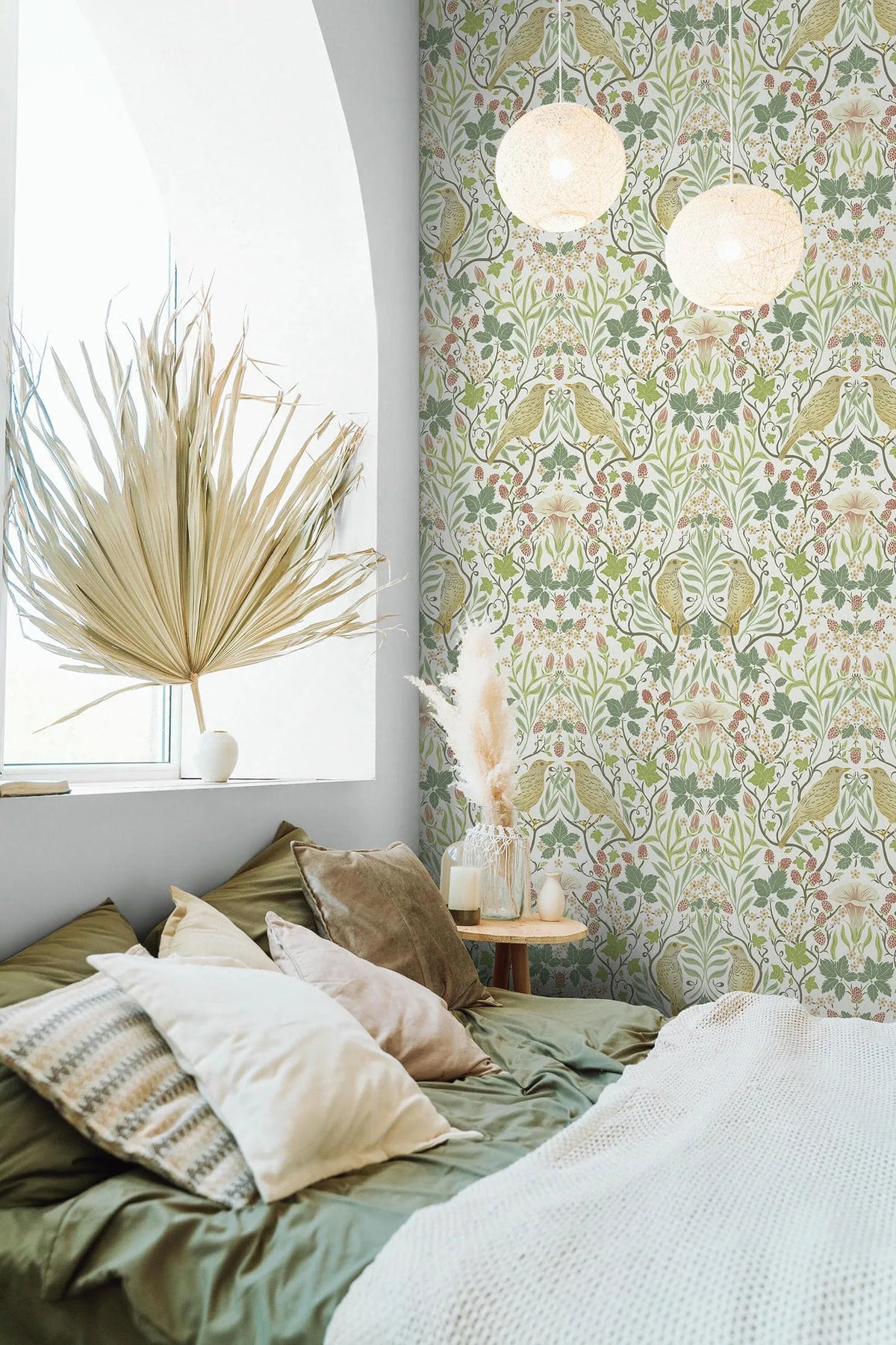 Marburg 47620 wallpaper serene bedroom feature wall behind a low bed with layered pillows, a round side table with pampas grass and candles, arched window and two pendant lights.