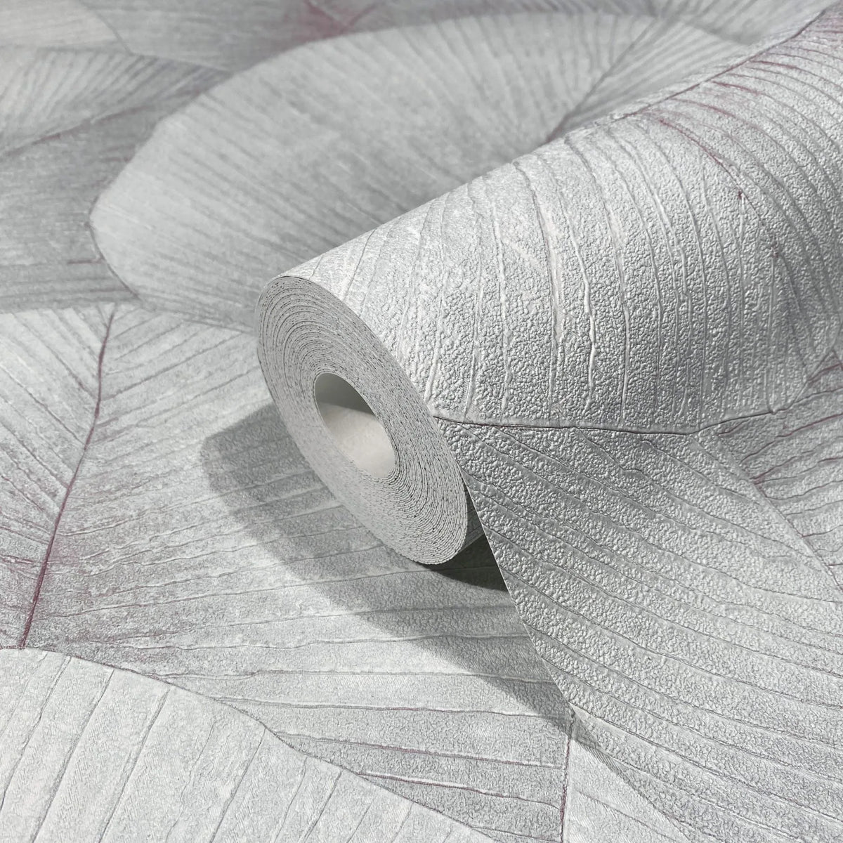 Marburg Kumano 34512 Close-up of a wallpaper roll resting on matching wallpaper showing a large overlapping leaf pattern with textured veins in light gray.