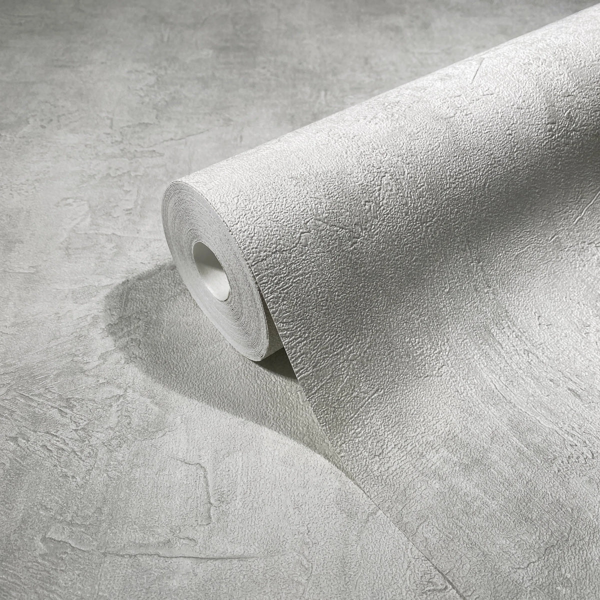Marburg Loft Superior 34192 Close-up of a light gray textured wallpaper roll unrolling across a matching surface, showing the plaster-like pattern.