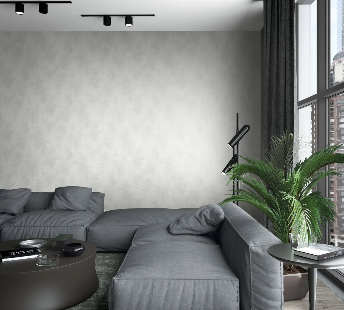 Marburg Loft Superior 34192 Light gray mottled wallpaper on a living room wall behind a low gray sectional sofa, with a round coffee table, side table with books, a black floor lamp, a potted palm, tall windows with dark curtains, and ceiling spotlights.