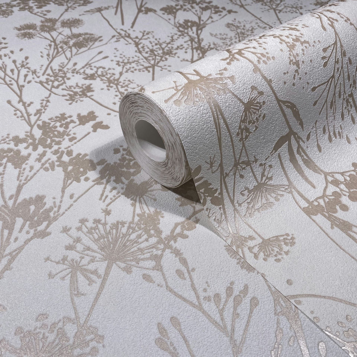 Marburg Mona 82463 Close-up of a wallpaper roll resting on matching wallpaper, showing beige botanical silhouettes of wildflowers on a textured white background.