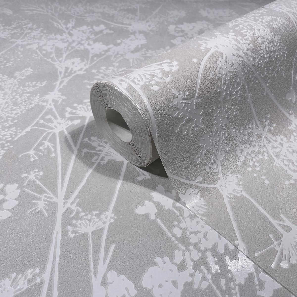Marburg Mona 82464 A wallpaper roll partially unrolled on a matching surface, showing a light gray textured ground with glossy white botanical silhouettes.