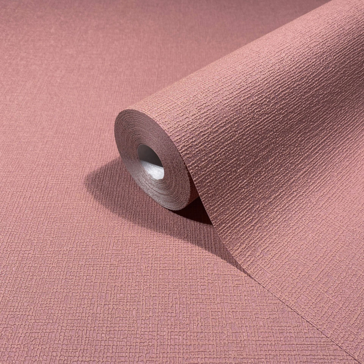 Marburg Mona 82467 A warm rose-red wallpaper roll with a fine embossed block texture, shown partially unrolled on the same material.