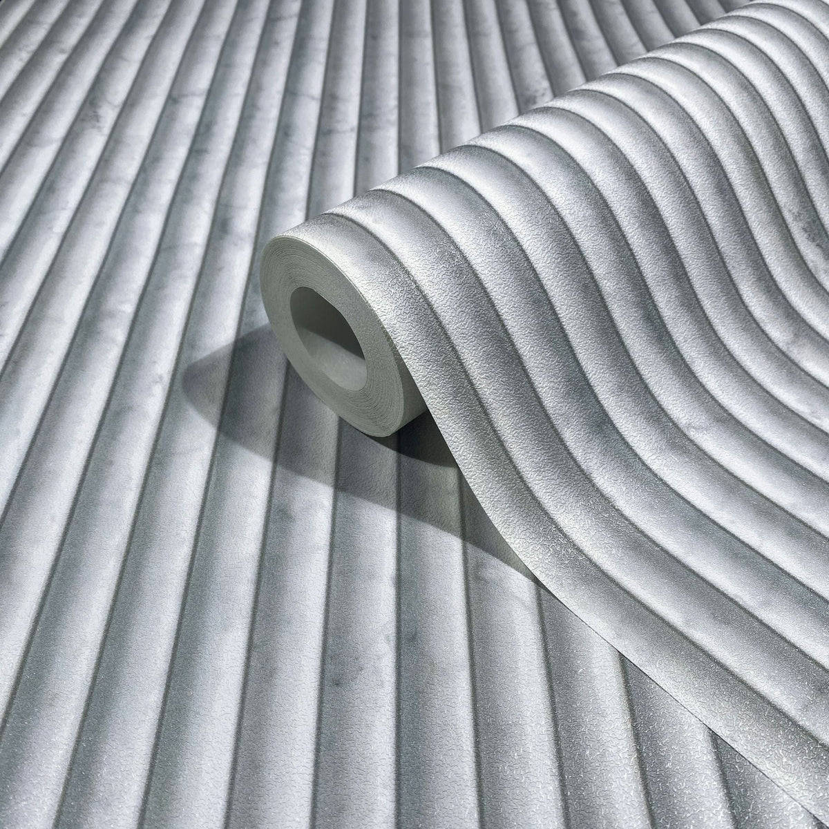 Marburg Mona 89005 A gray wallpaper roll with softly curved vertical ribs, shown resting on the same patterned wallpaper.