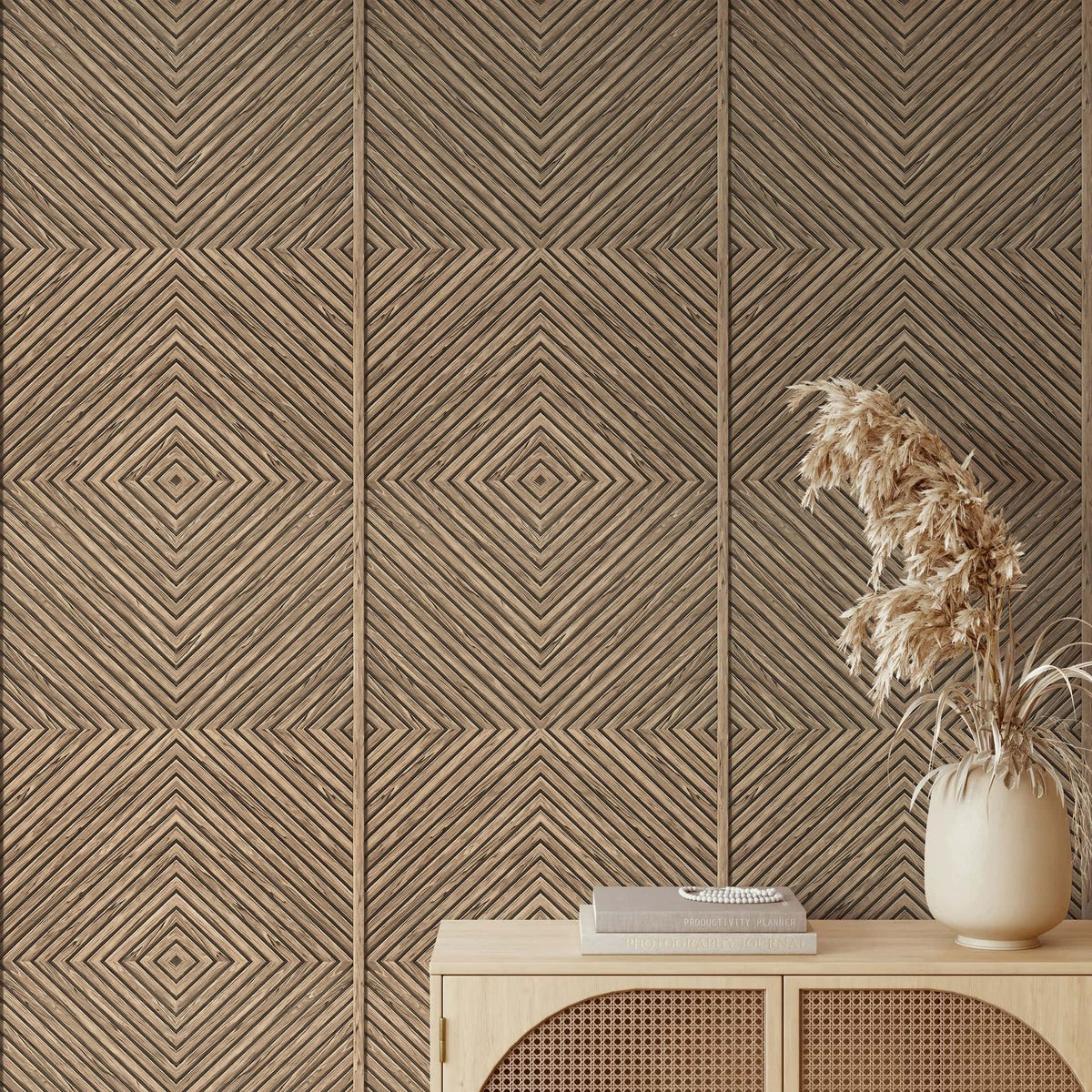 Marburg Naomi 89019 Beige geometric wallpaper with diagonal lines forming nested diamonds, shown behind a light wood console with stacked books and a ceramic vase of dried grasses.