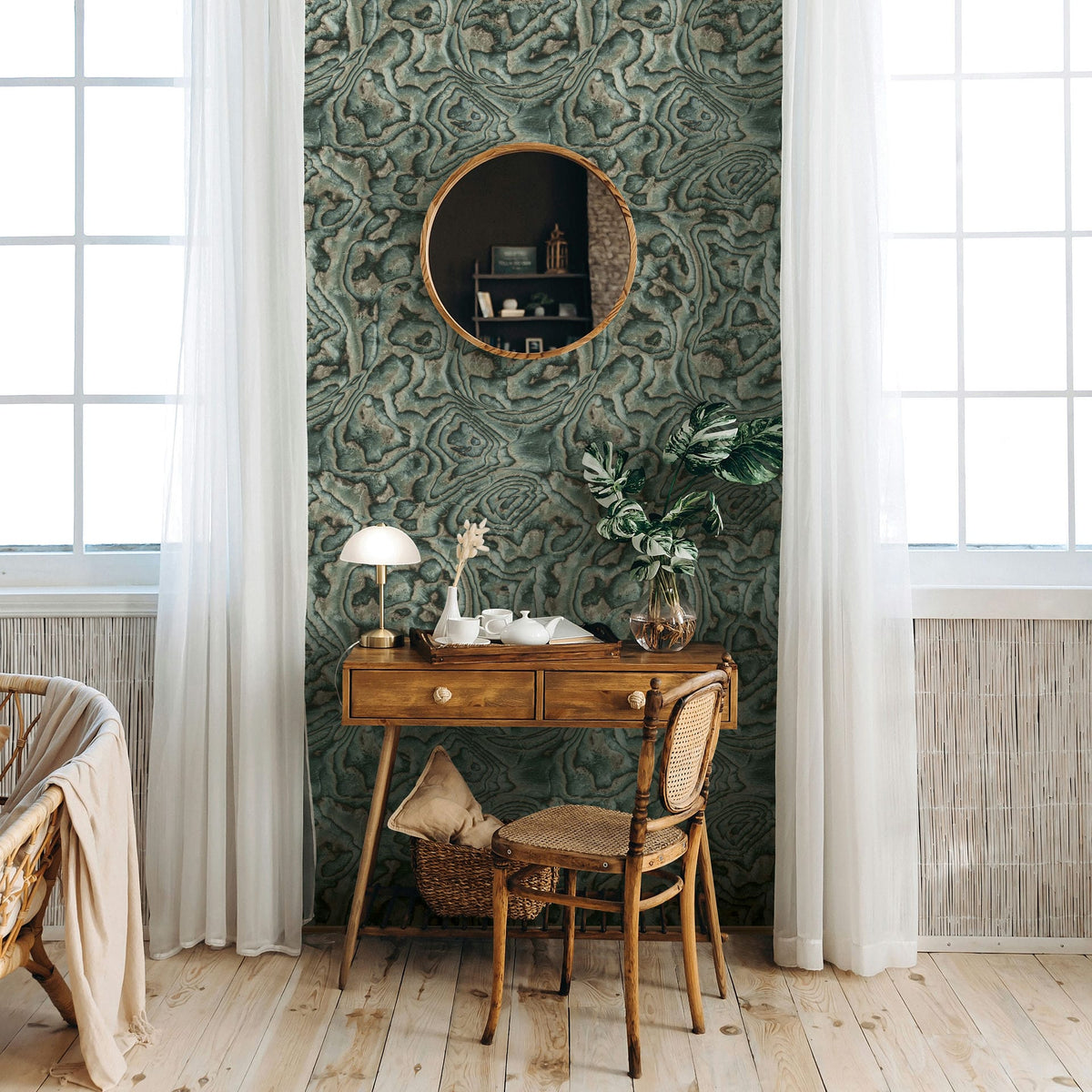 Marburg Novamur Mona 81691 Green and gray abstract swirled wallpaper used as a feature wall behind a wooden desk with a round mirror, windows, and sheer curtains.