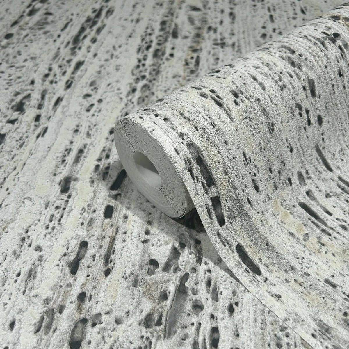 Marburg Travertino 33350 Close-up of a partially unrolled wallpaper roll showing a beige and gray stone-effect, pitted texture pattern.