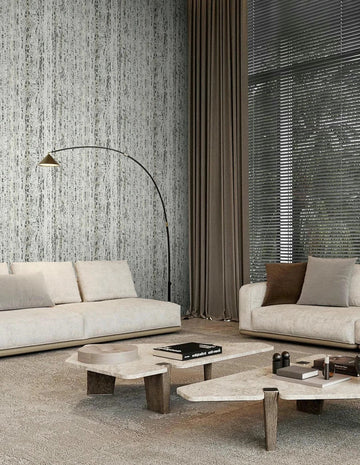 Marburg Travertino 33350 Modern living room featuring a beige and gray vertical striated wallpaper on the feature wall behind two light sofas, with an arc floor lamp, nesting coffee tables with books, tall curtains, and window blinds.