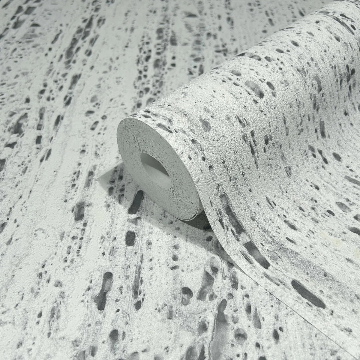 Marburg Travertino 33352 A wallpaper roll partially unrolled on matching material, showing a gray and white travertine stone–look pattern with irregular streaks and pits.