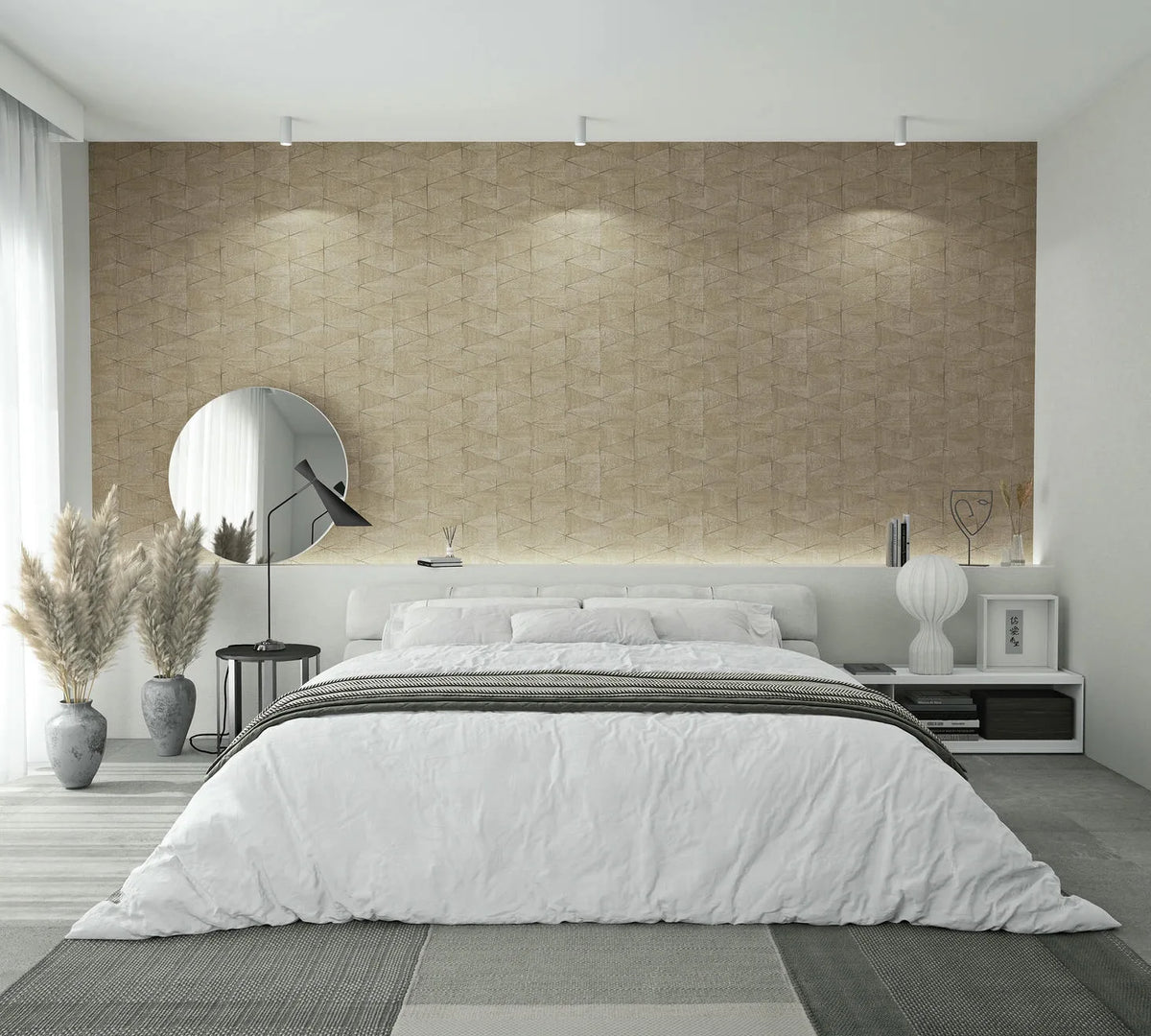 Marburg Travertino 33359 Bedroom scene featuring a beige geometric textured wallpaper feature wall behind a low bed with white bedding, a round mirror and black side table with lamp on the left, floor vases with pampas grass, and a white nightstand with a ribbed lamp on the right.