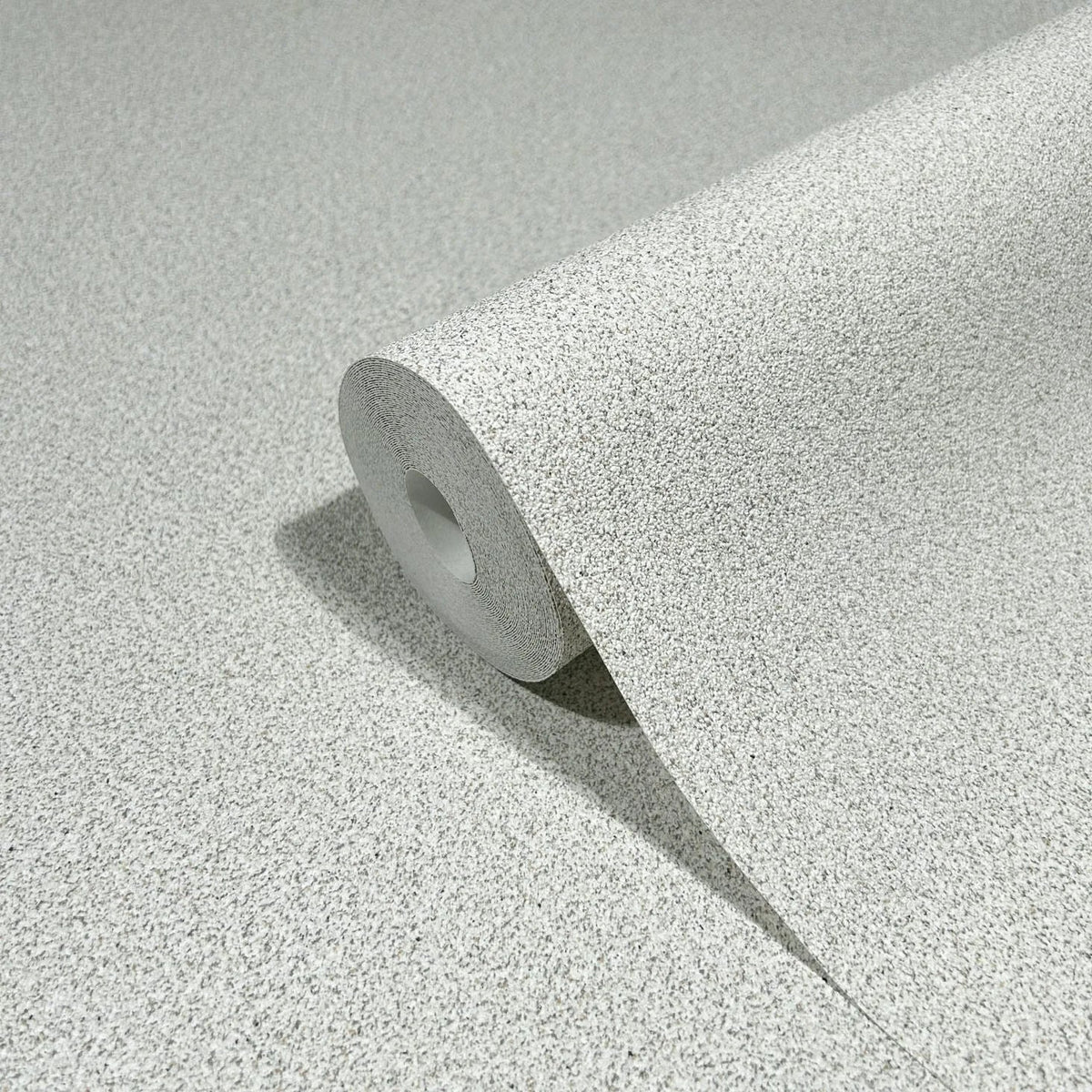 Marburg Travertino 33362 A wallpaper roll with a light gray and beige speckled texture, partially unrolled on a matching surface.