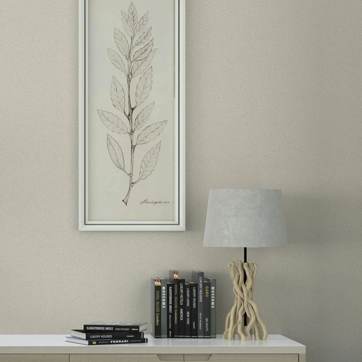 Marburg Travertino 33363 Light beige textured wallpaper behind a modern sideboard styled with stacked books, a sculptural table lamp, and a tall framed leaf illustration.
