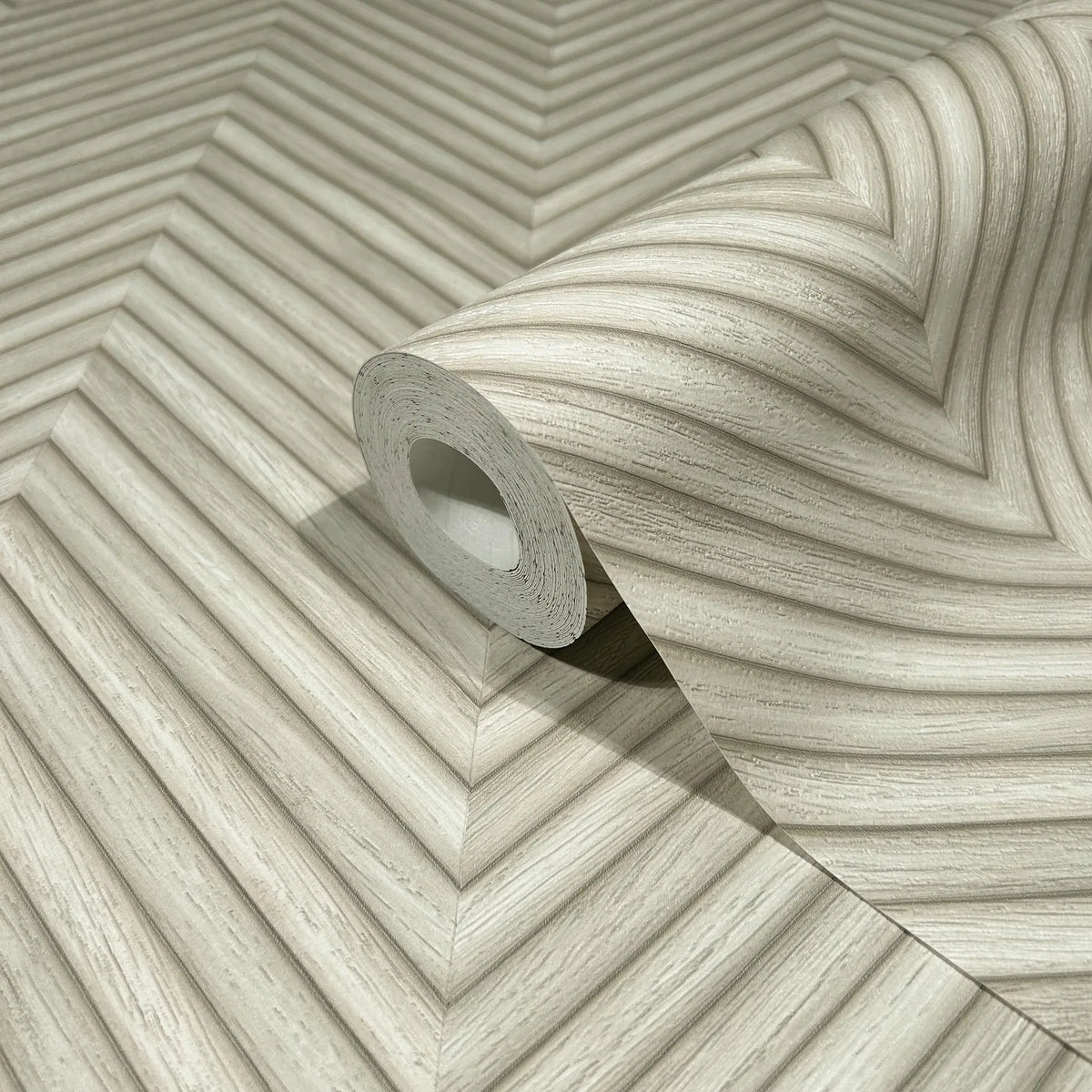 Marburg Travertino 33373 A wallpaper roll resting on matching beige chevron-patterned paper with fine striated lines forming V-shaped bands.