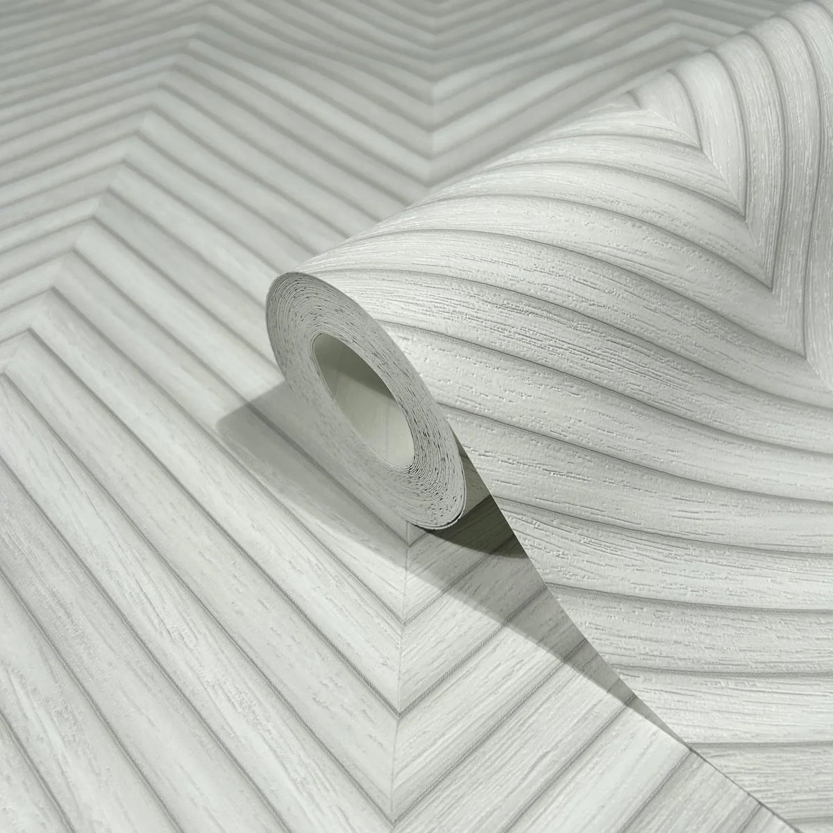 Marburg Travertino 33375 Close-up of a wallpaper roll resting on matching wallpaper showing a light gray and white chevron pattern with fine linear texture.