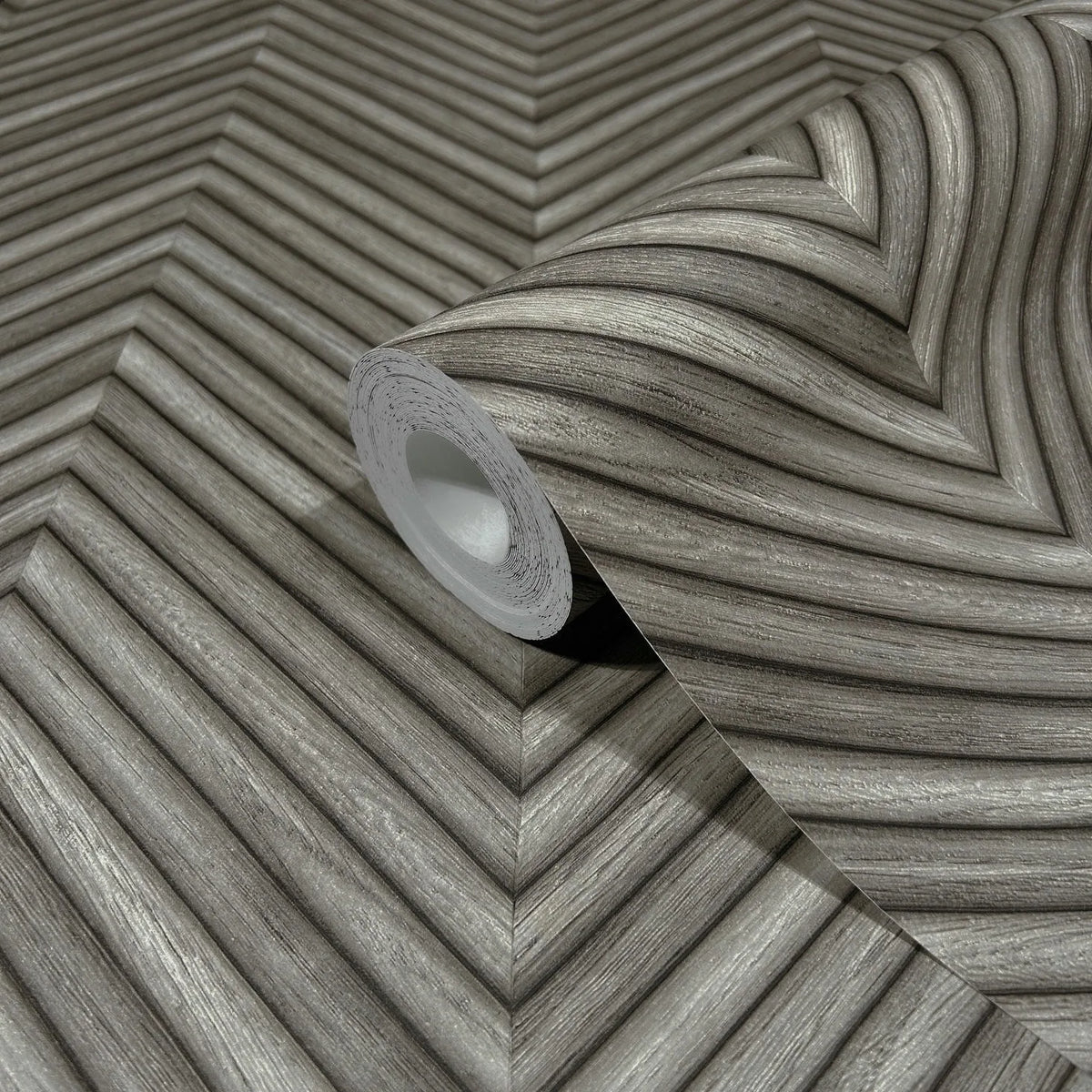 Marburg Travertino 33380 A gray wallpaper roll on a matching unrolled sheet showing a dimensional chevron pattern with woodgrain-like striations.
