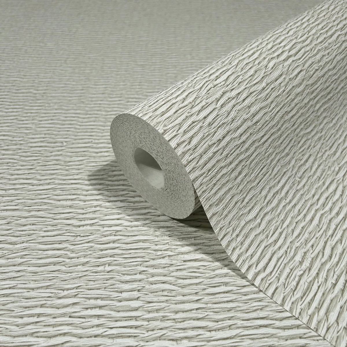 Marburg Travertino 33382 Close-up of a wallpaper roll with raised, wavy linear texture in light beige, resting on a matching unrolled sheet.