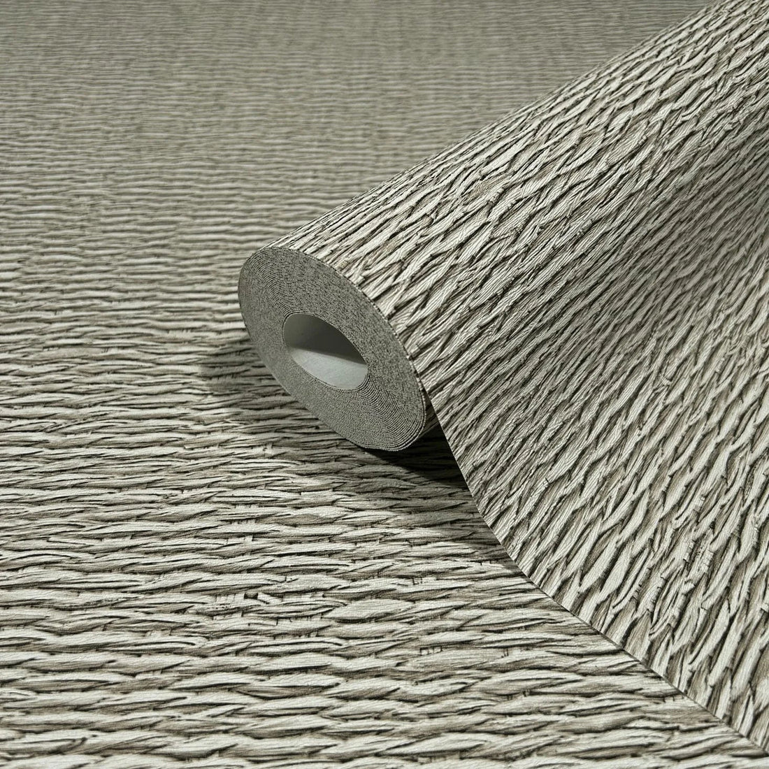 Marburg Travertino 33383 Textured beige wallpaper with narrow horizontal ridges behind three gray stone vases on a light stone surface.