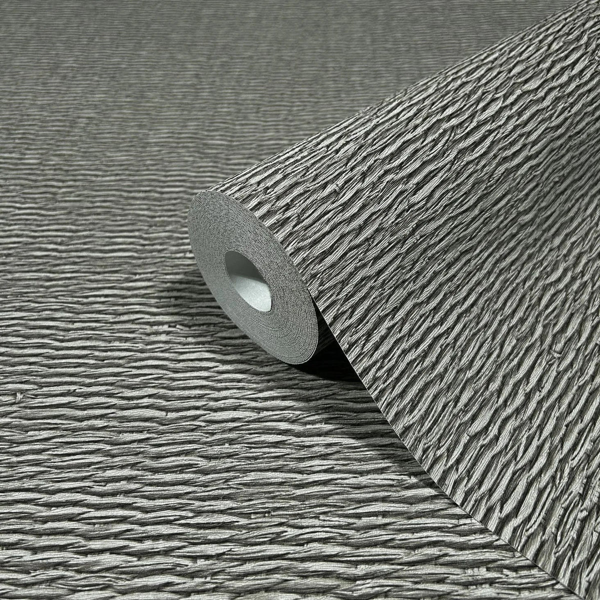 Marburg Travertino 33386 Close-up of a gray wallpaper roll with raised horizontal ridges, resting on the same textured pattern.